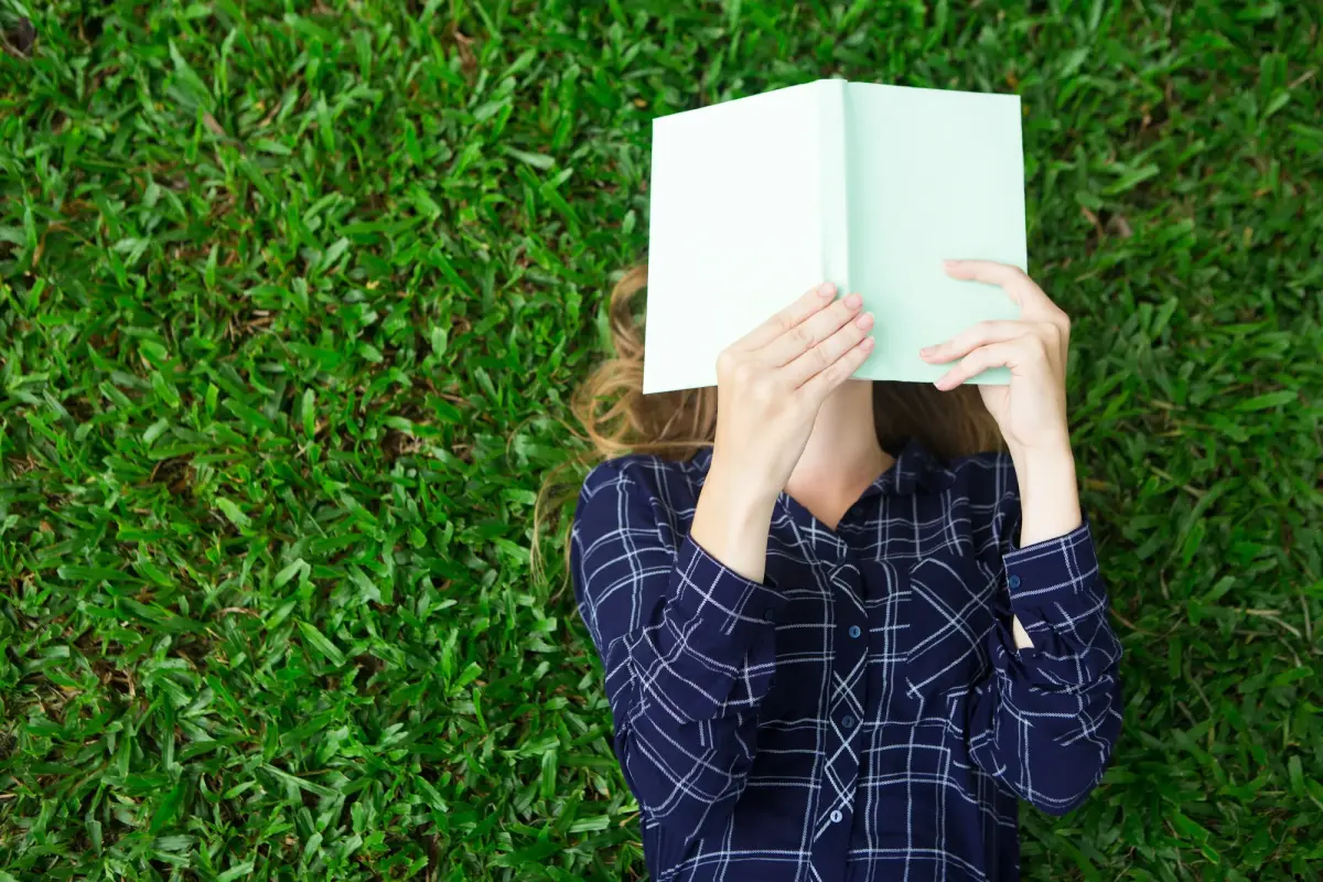 Eine Frau liegt im Gras und hält ein aufgeschlagenes Buch vor ihr Gesicht – kurz vor dem Buch veröffentlichen.