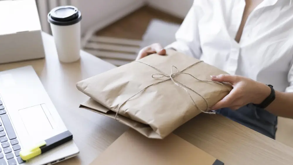 Eine Person hält ein Paket in der Hand, während sie an einem Tisch im Verkaufsprozess arbeitet.
