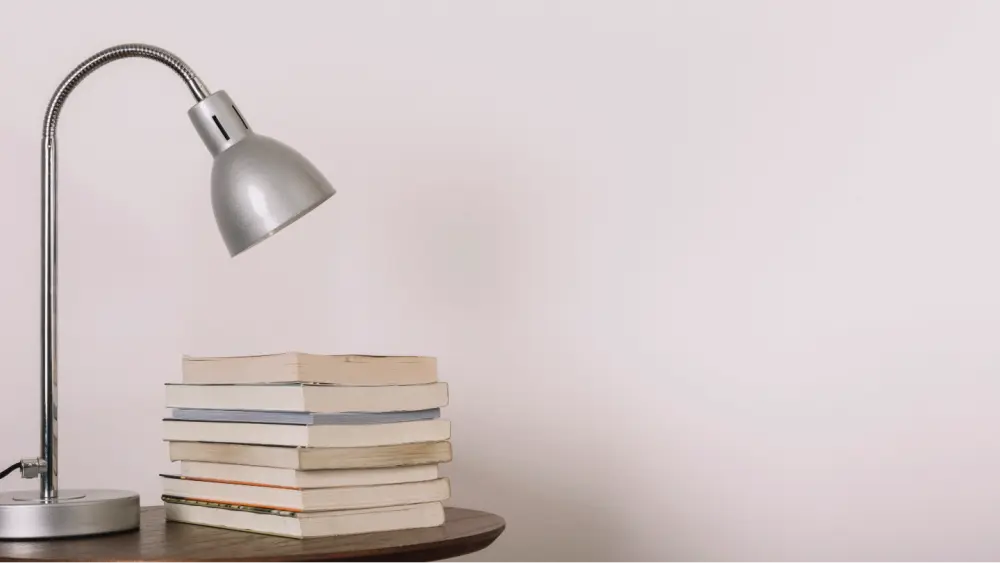Ein Stapel Bücher und eine Lampe auf einem Tisch, passend zum Thema Druckkostenzuschuss Verlag.