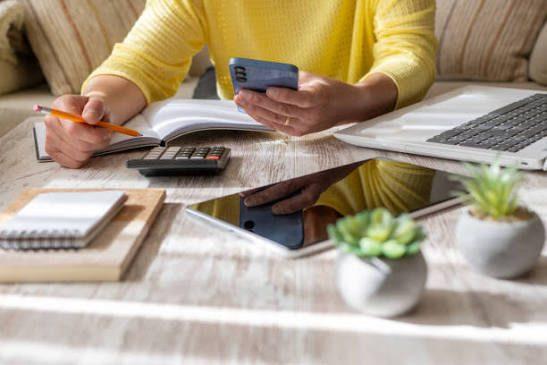 Eine Person berechnet ihre Rentenlücke mit Smartphone und Rechner.