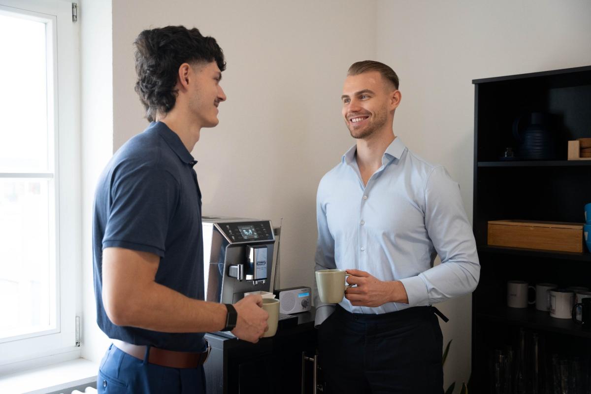 Zwei Männer unterhalten sich lächelnd bei einer Tasse Kaffee über die Riester-Rente.