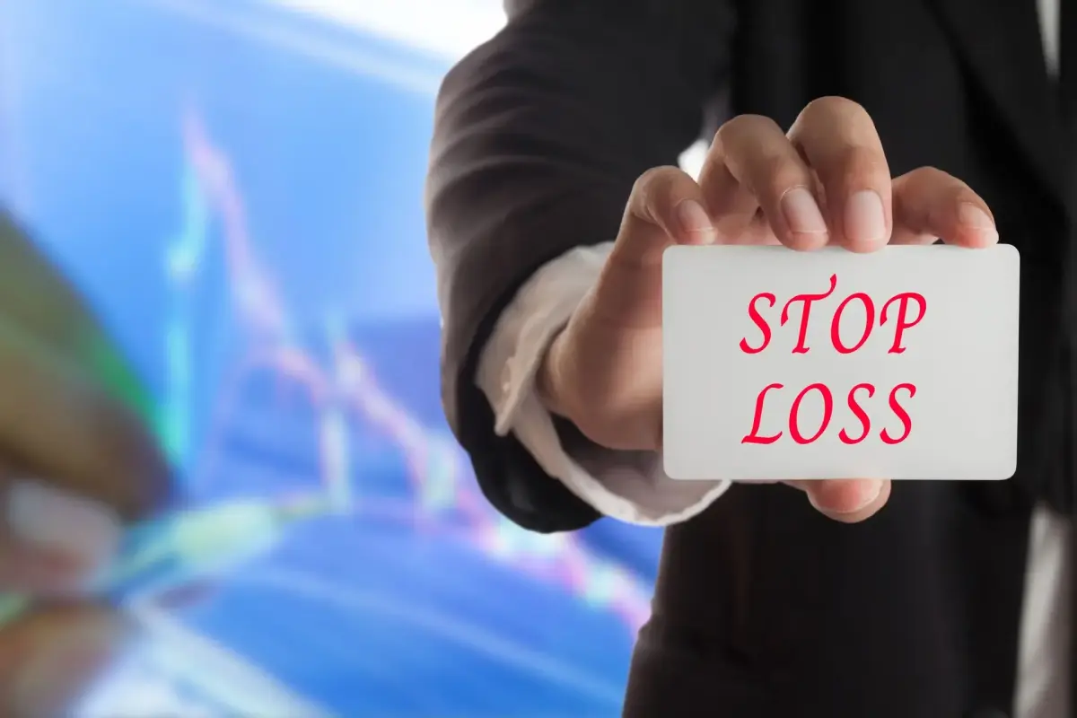 Eine Hand hält ein Stop-Loss-Schild vor einem Finanzdiagramm im Trading.