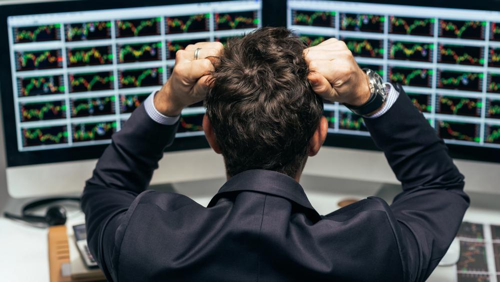 Ein frustrierter Trader mitunter auf die Psychologie des Tradings, der vor seinen Monitoren sitzt.