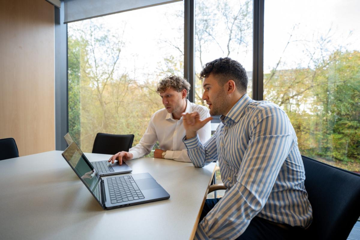 Zwei Männer besprechen Statistik lernen neben Job, während sie auf einen Laptop schauen.