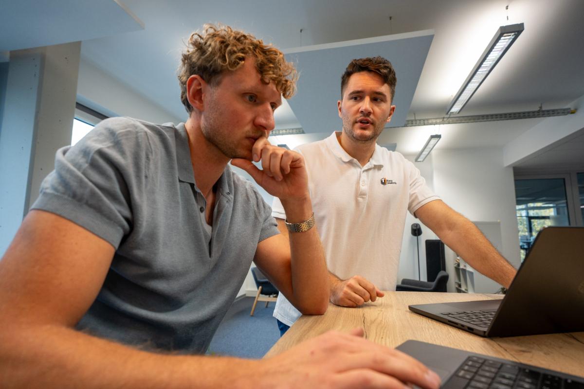 Zwei Männer analysieren Finanzdaten am Laptop in einem modernen Büro.