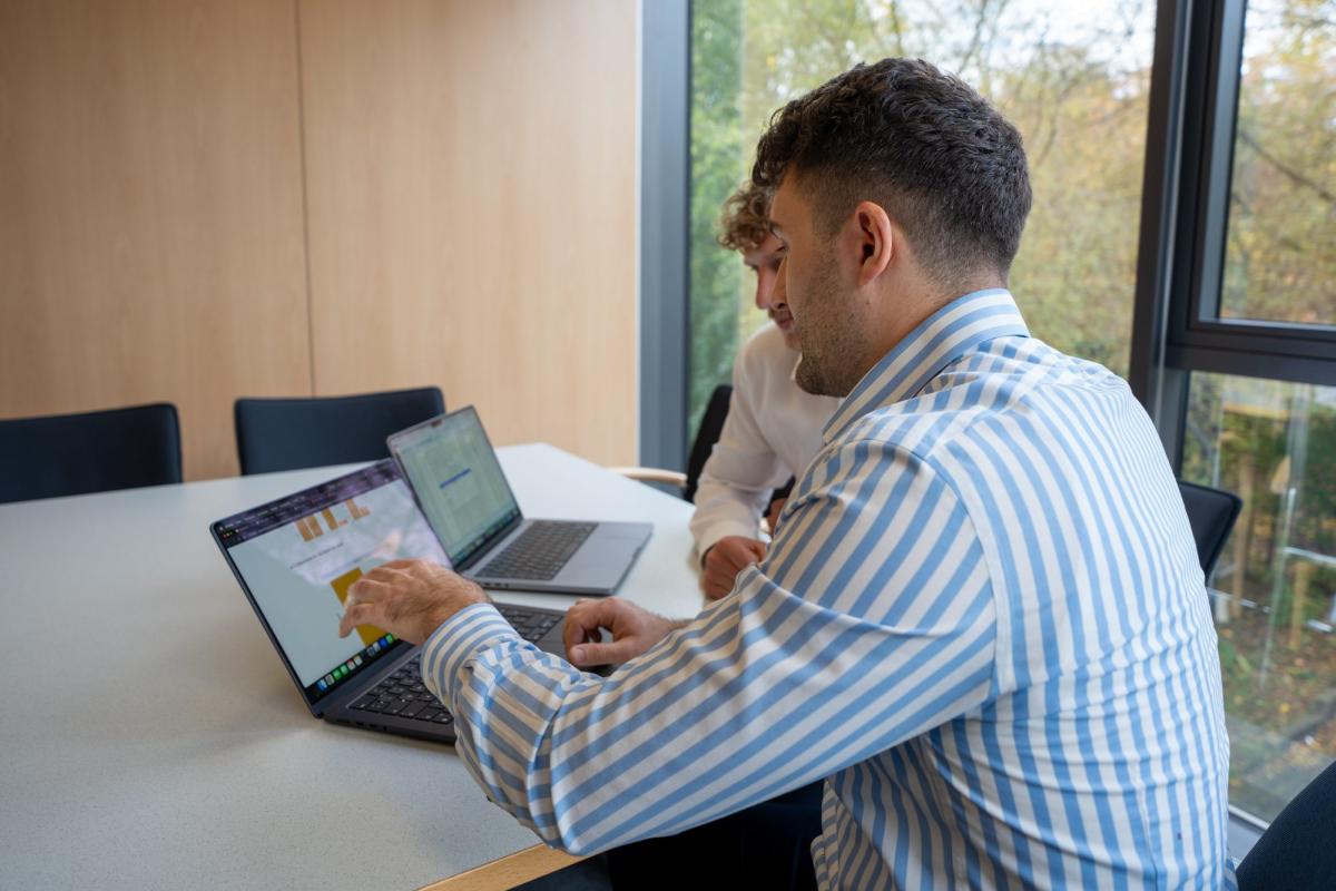 Zwei Personen analysieren Odds Ratios auf Laptops in einem Besprechungsraum.
