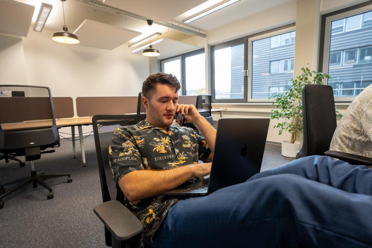 Ein Mann analysiert seine Daten auf einem Laptop in einem modernen Büro während eines Telefonats.