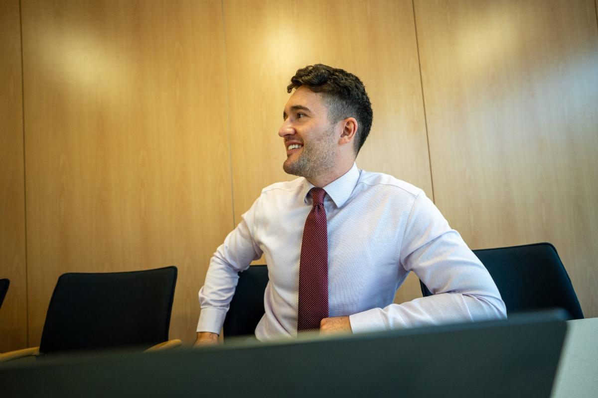 Junger Mann in Anzug, der an einem Tisch sitzt und über Statistik selbst auswerten lächelt.