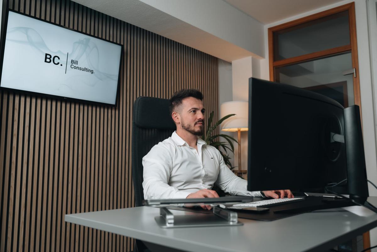 Agentur Business am Arbeitsplatz: Ein Mitarbeiter arbeitet am Schreibtisch vor einem großen Monitor.