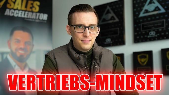 Mann mit Brille und Westen spricht über Vertriebs-Mindset im Büro.