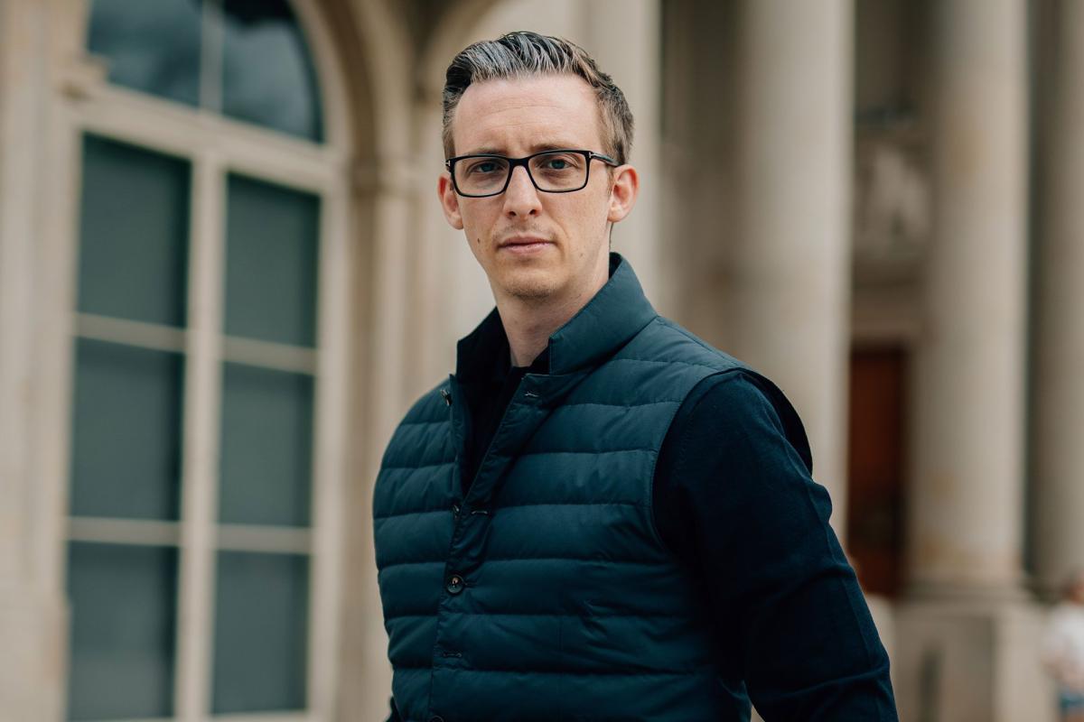 Ein Mann mit Brille steht vor einem historischen Gebäude und denkt über B2B-Vertrieb optimieren nach.