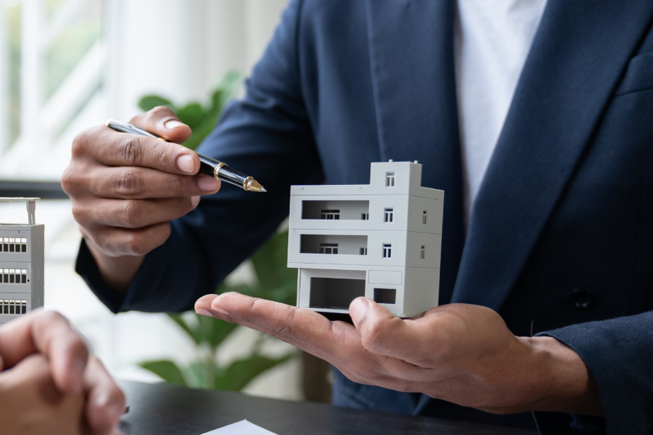 Ein Immobilienberater erklärt die Gebäudeversicherung in Mainz anhand eines Modellgebäudes.