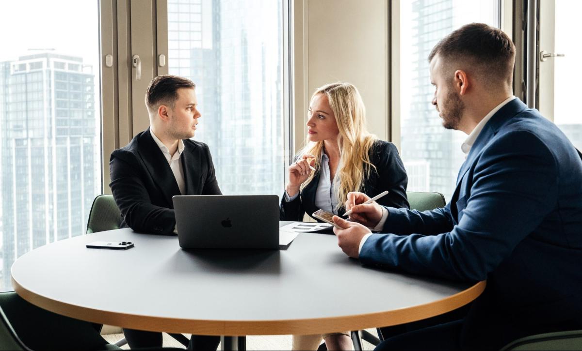 Drei Personen in einem Büro diskutieren über Aktien-Investments in einer Holding.