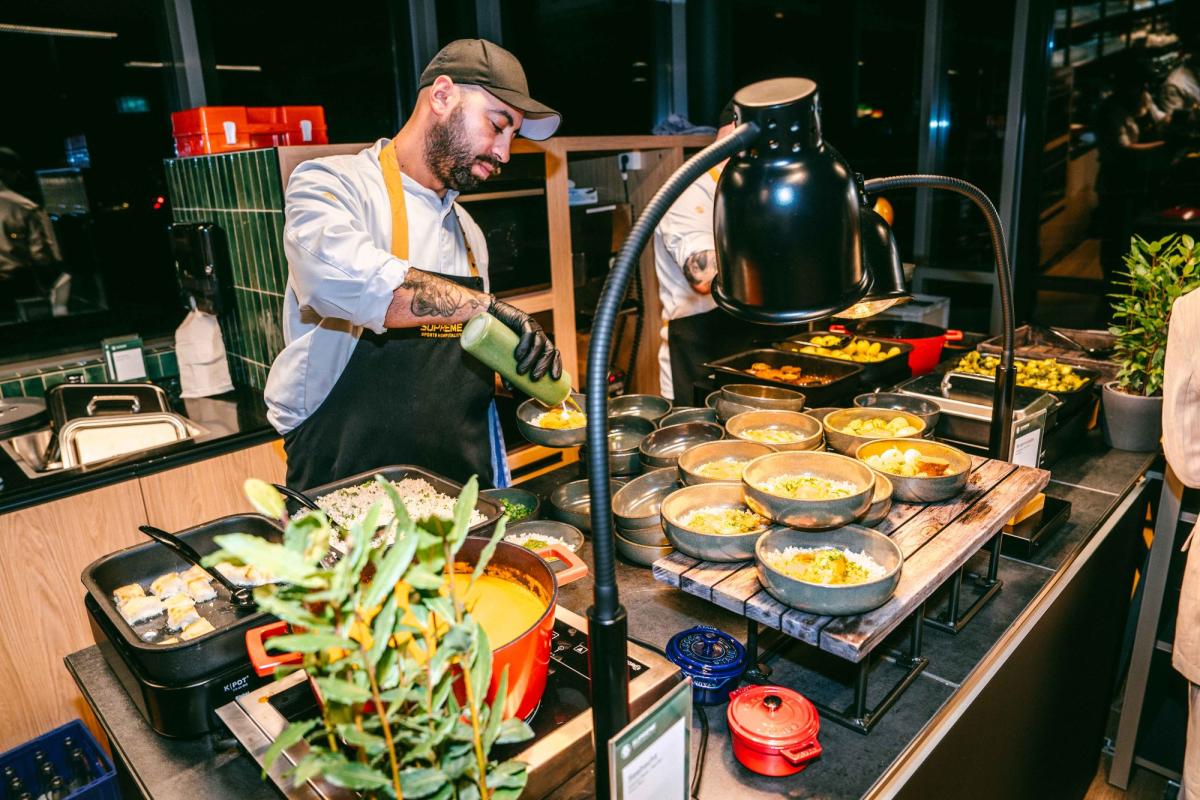 Ein Koch bereitet beim Catering für ein Firmenevent verschiedene Gerichte an einer Buffetstation.