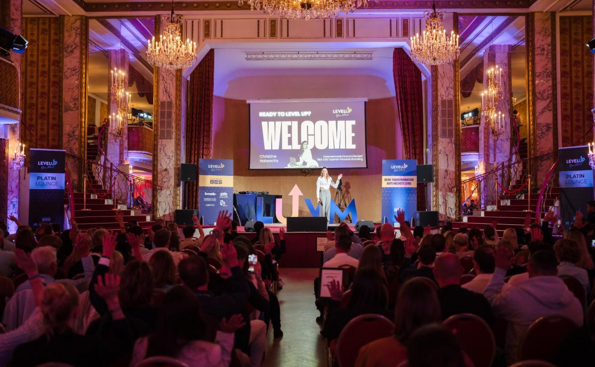 Die Bühne eines Events zeigt den Schriftzug 'WELCOME' und ein Publikum.