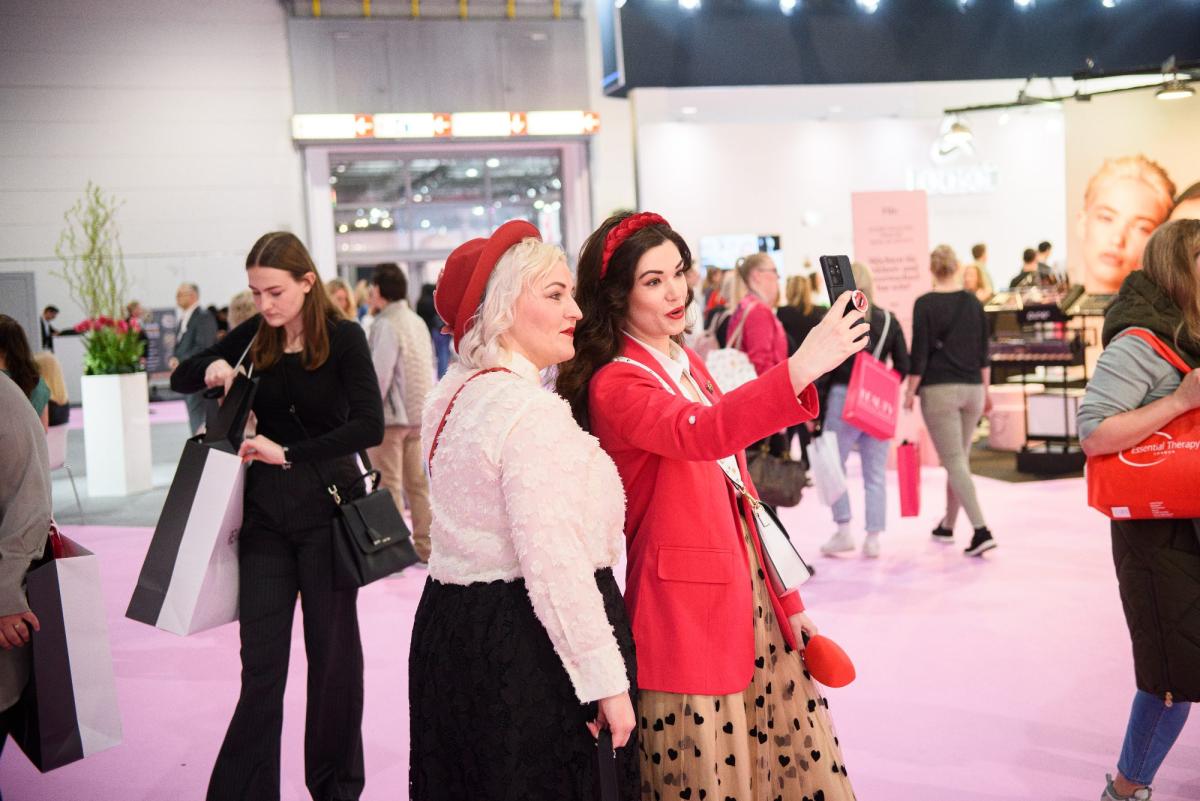 Zwei Frauen machen ein Selfie während einer Beauty-Messe, um Marketing für Kosmetikerinnen zu zeigen.