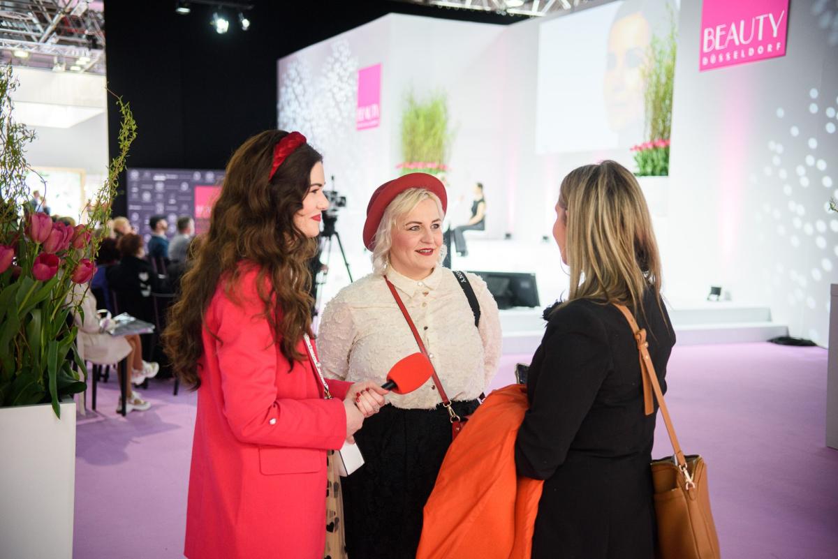 Drei Frauen sprechen auf einer Messe über Beauty Business Consulting.