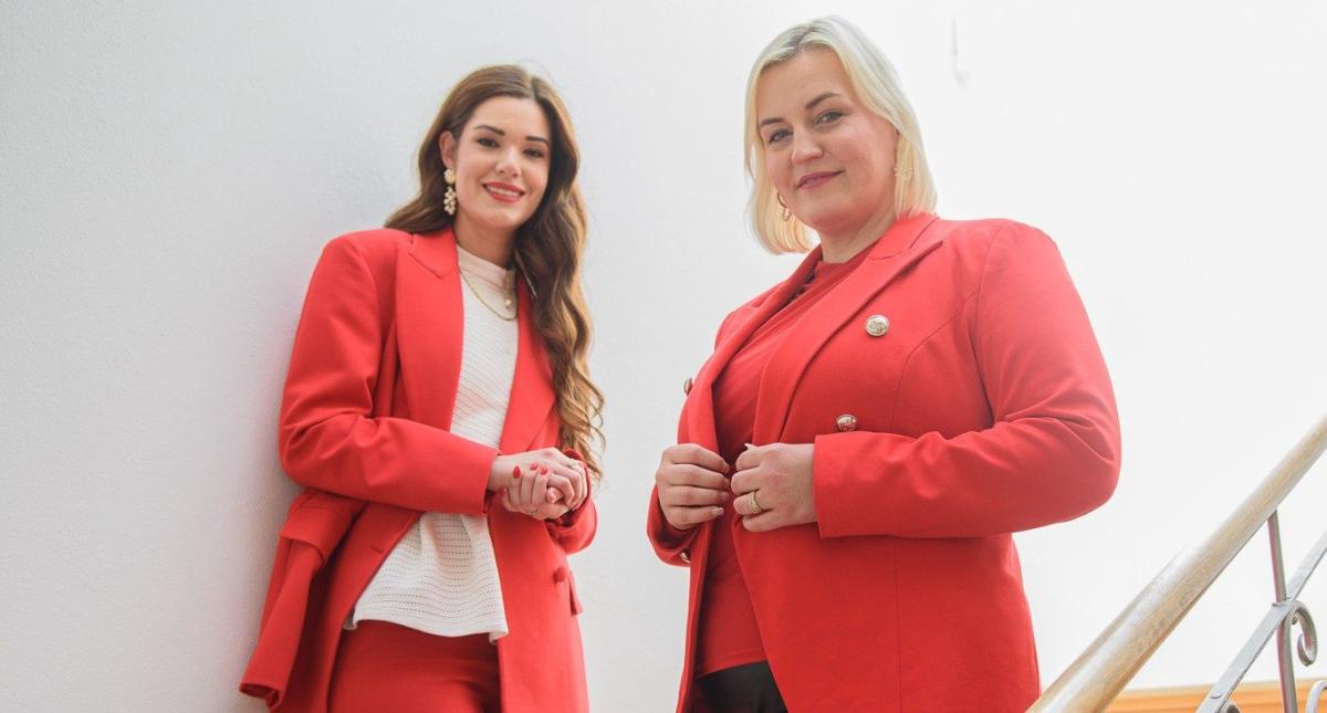 Zwei Frauen in roten Blazern stehen in einem Kosmetikstudio und beraten.