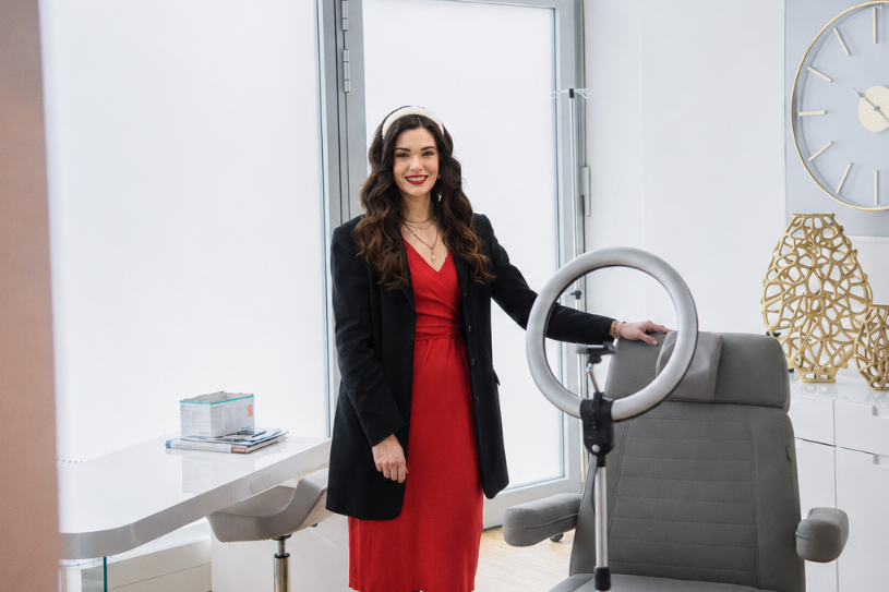 Frau in rotem Kleid im Kosmetikstudio mit Behandlungsstuhl, der das Thema Künstliche Intelligenz im Kosmetikstudio aufgreift.
