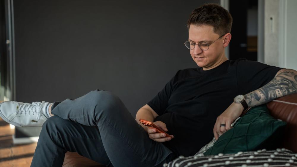 Ein Mann sitzt entspannt auf dem Sofa und prüft sein Smartphone, um LinkedIn effektiv zu nutzen.