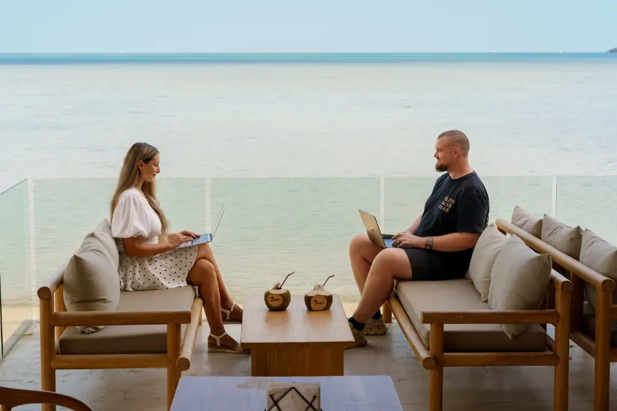 Zwei Menschen arbeiten an Laptops im Nebenerwerb am Strand.