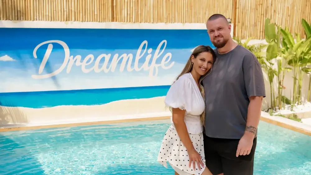 Ein Paar steht am Pool und zeigt mit lächelnden Gesichtern einen Nebenerwerb Lebensstil.
