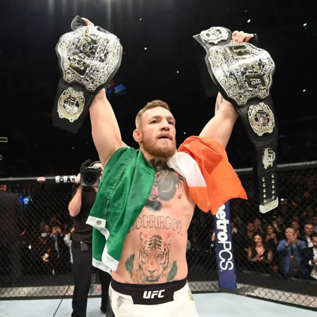 Conor McGregor feiert mit zwei UFC-Meisterschaften und der irischen Flagge.