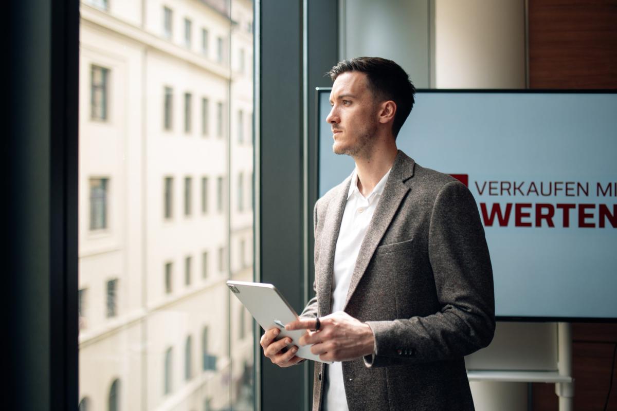 Mann im Anzug hält ein Tablet und blickt nachdenklich aus dem Fenster, LinkedIn-Content-System.