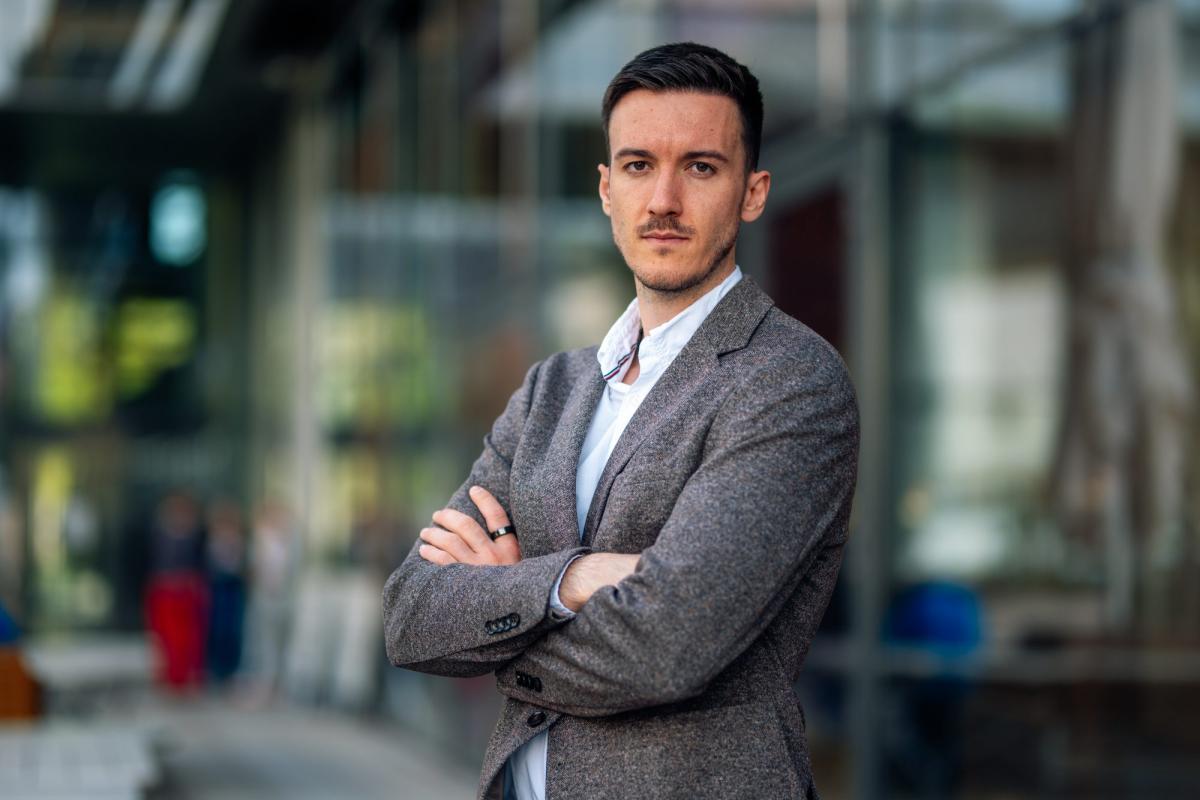 Webinare für Coaches im Büro: Ein Coach steht mit verschränkten Armen in einem modernen Glasgebäude.