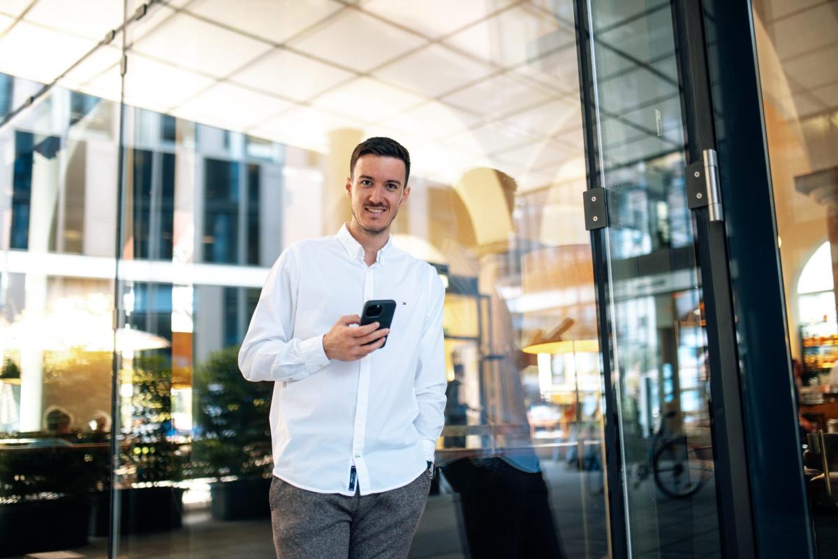 Mann mit Smartphone vor einem modernen Gebäude, das LinkedIn-Kunden gewinnen möchte.