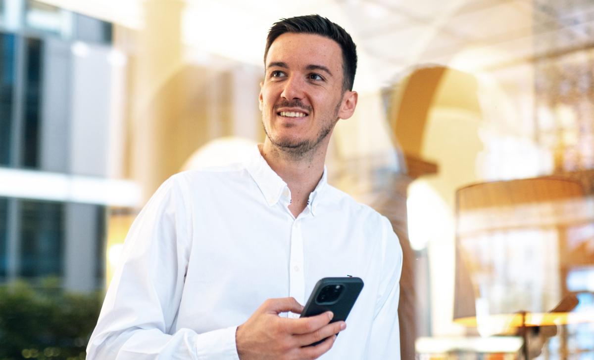 Mann mit Smartphone denkt über seine Geld mindset coaching nach.