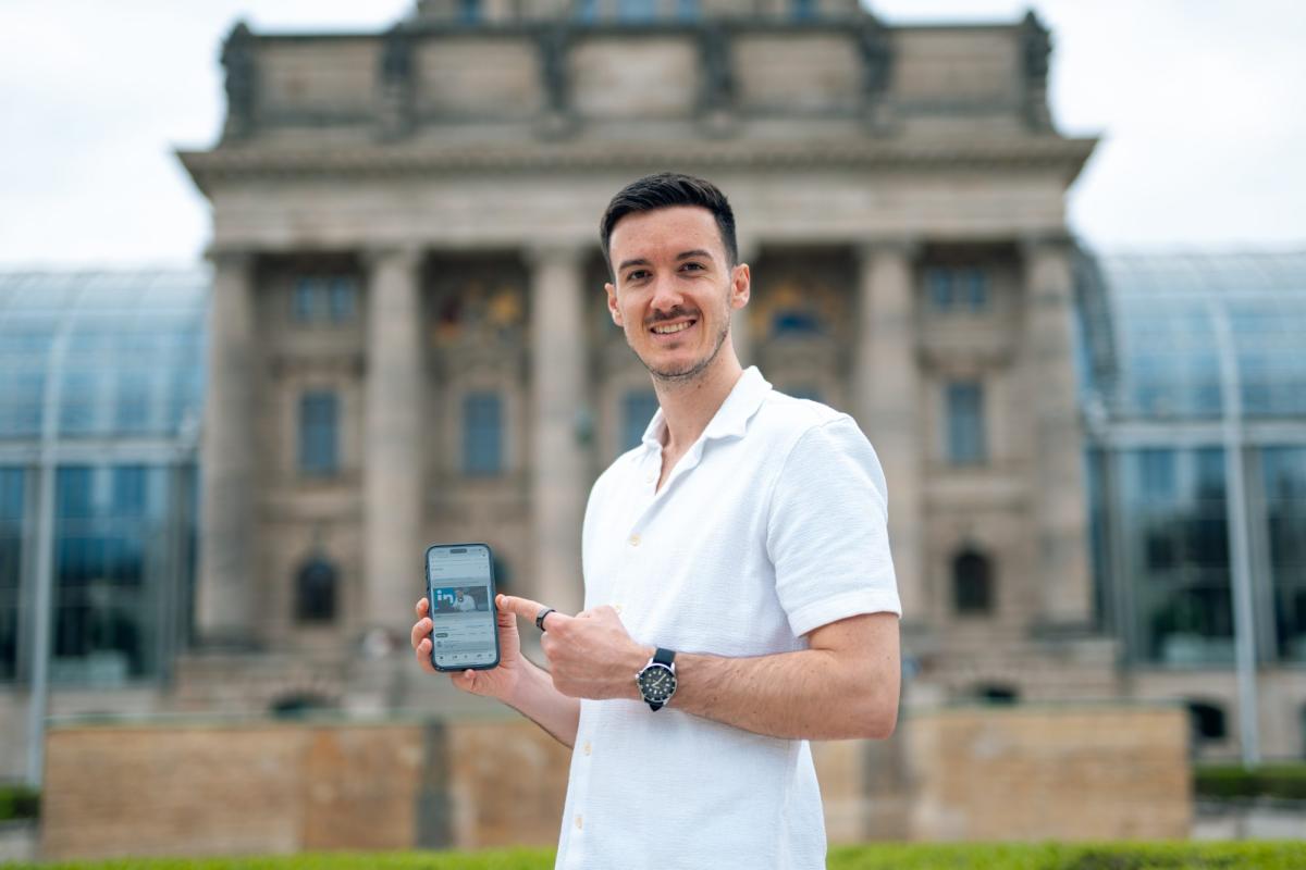 Mann zeigt auf Smartphone und spricht über Scam Coaches vor einem Gebäude.