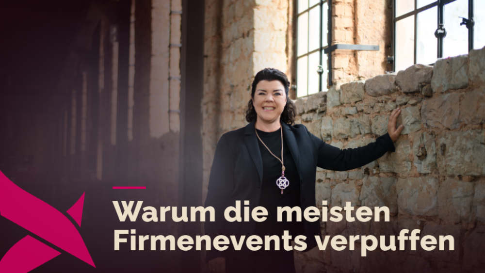 Eine lächelnde Frau steht neben einer alten Steinmauer in einer Industriehalle. Firmenevents stehen als Thema im Bild.