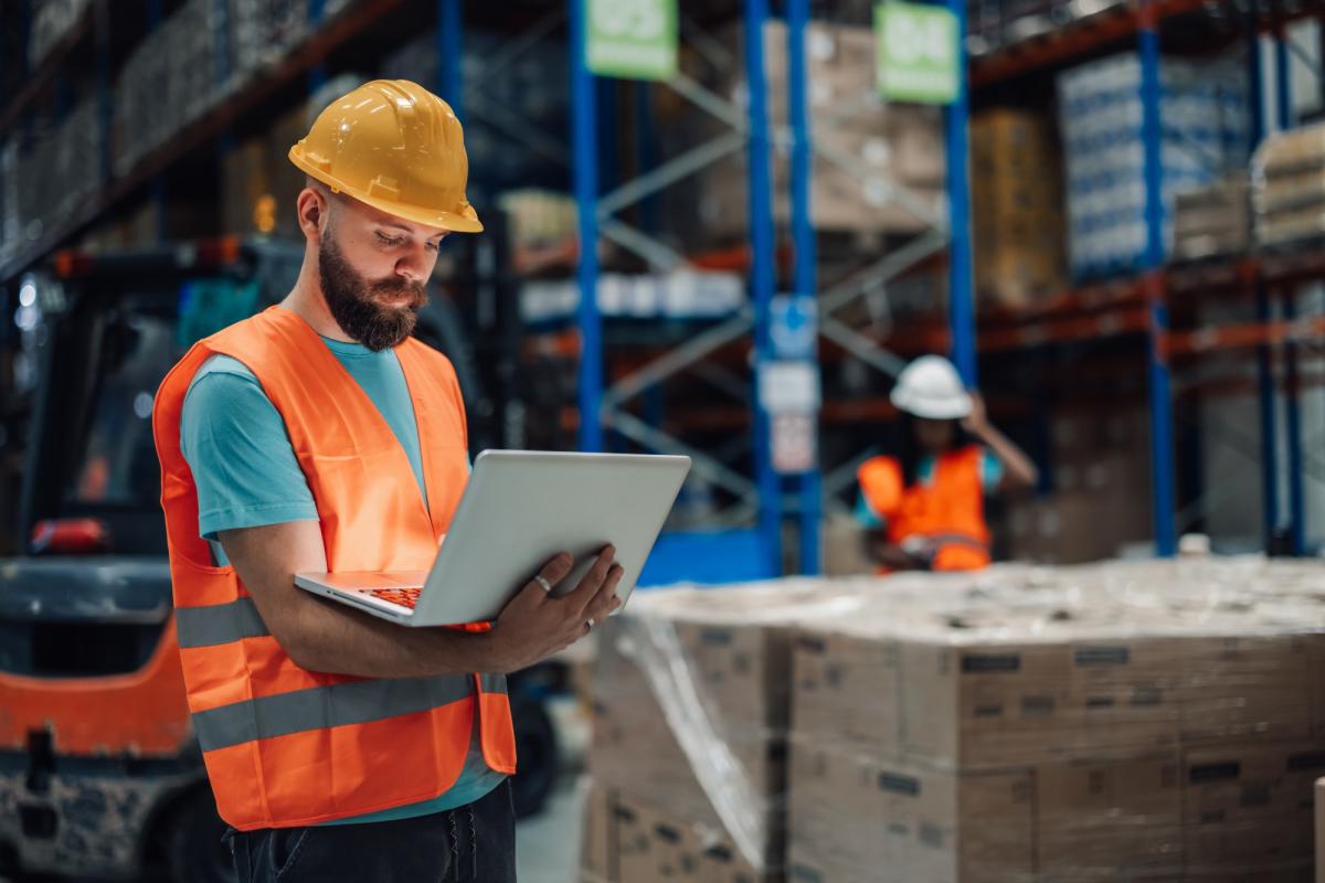 Mitarbeiter prüft im Lager mit einem Tablet Paletten und Warenbestände – SAP-Logistik im Arbeitsalltag.