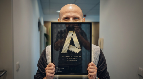 Michael Bendl hält Top Arbeitgeber Award von fairfamily in die Kamera