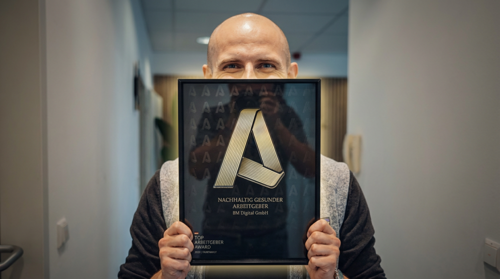Michael Bendl hält Top Arbeitgeber Award von fairfamily in die Kamera