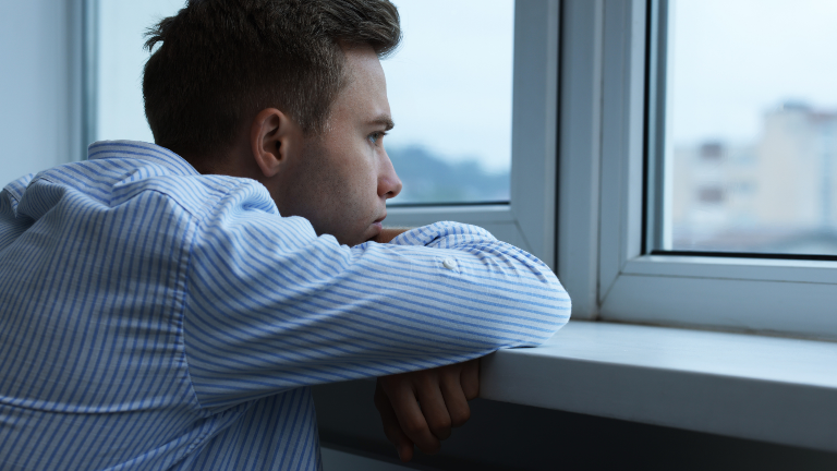 Nachdenklicher Mann, der am Fenster sitzt und über seinen Sissy-Fetisch nachdenkt.