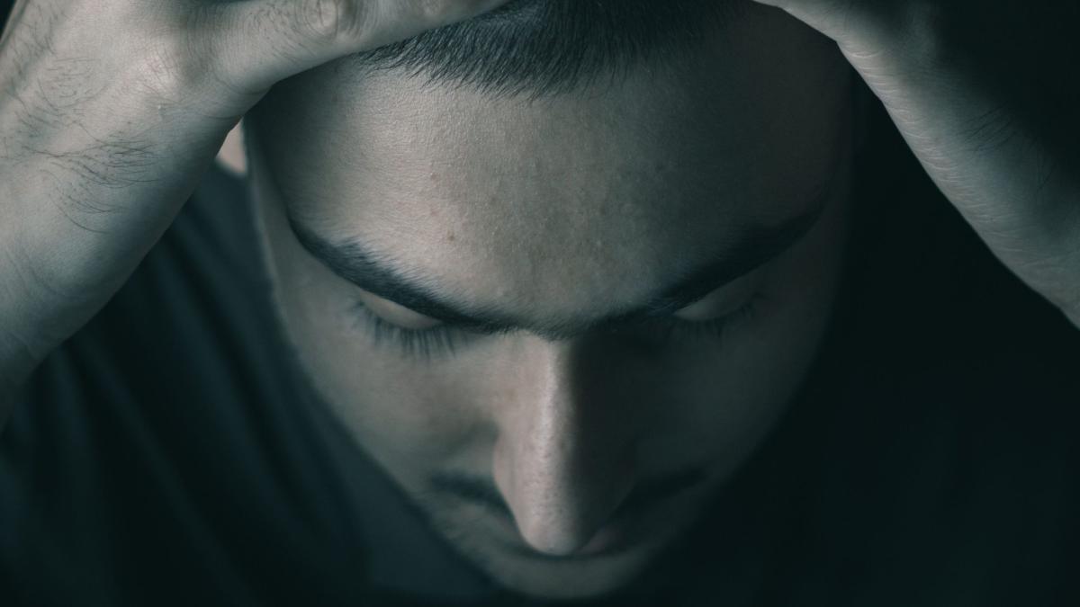 Gestresster Mann mit verschlossenen Augen, der an der Zwanghaften Masturbation überwinden möchte.