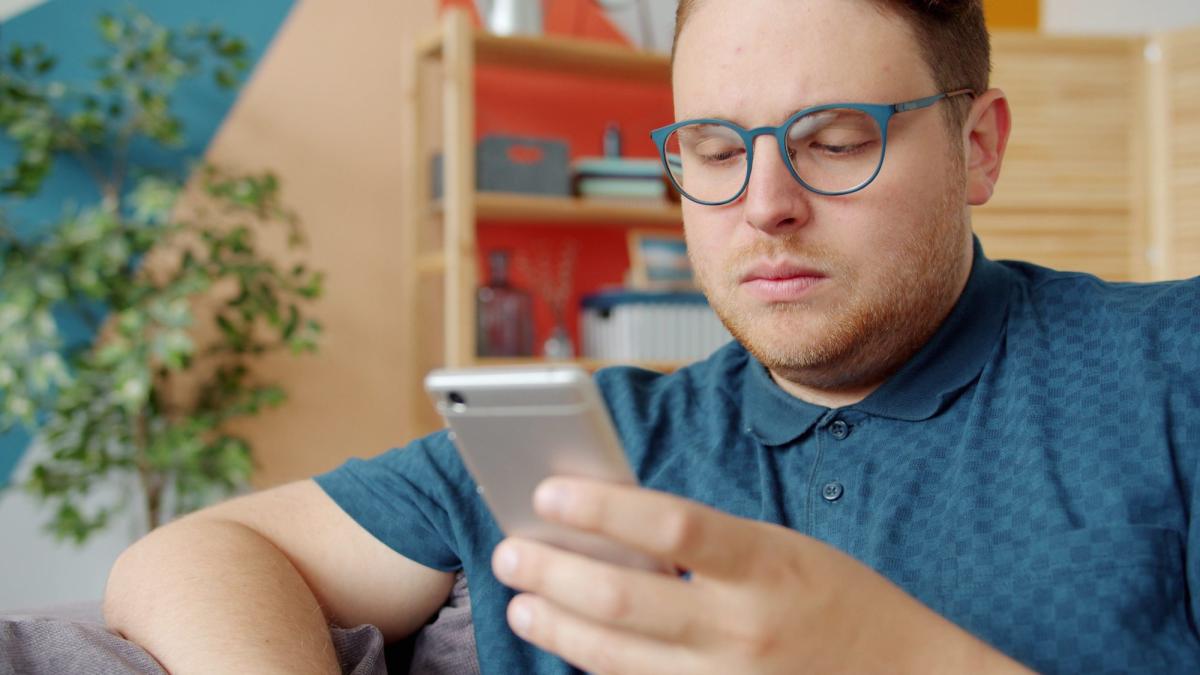 Mann mit Brille liest auf seinem Smartphone über den Trans-Fetisch loswerden.