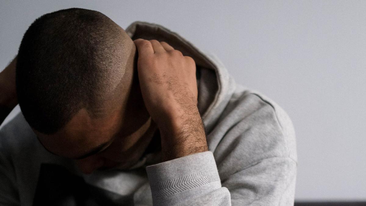 Ein Mann in grauem Hoodie sitzt mit gesenktem Kopf und verdeckt teilweise sein Gesicht, Thema: Trans-Fetisch loswerden.