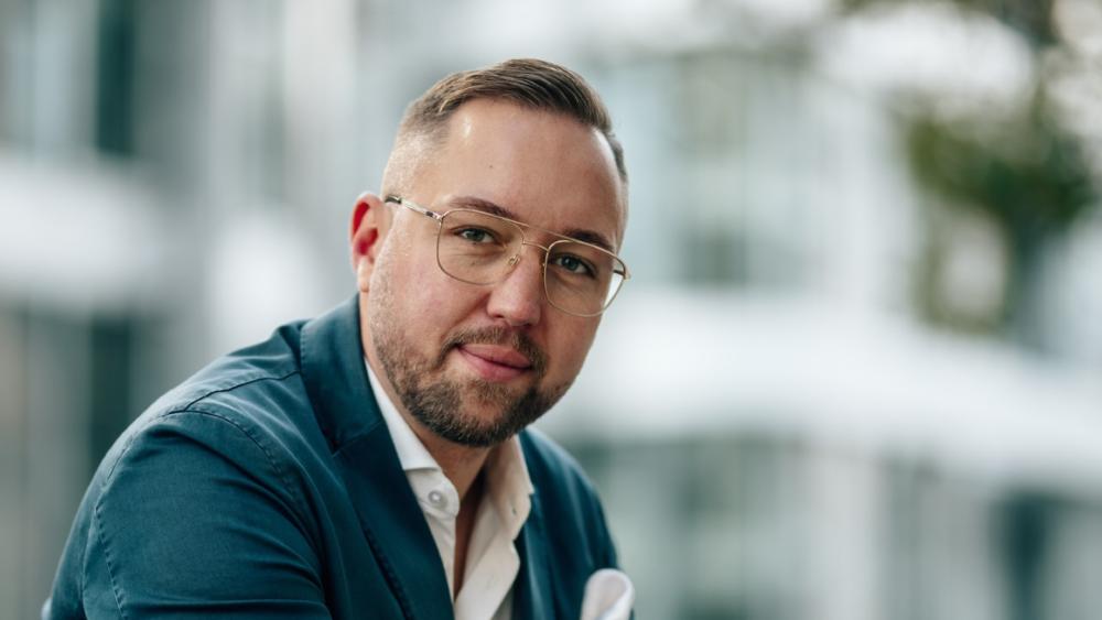 Mann mit Brille und Anzug zeigt, wie Vermögensaufbau für Gutverdiener funktioniert.