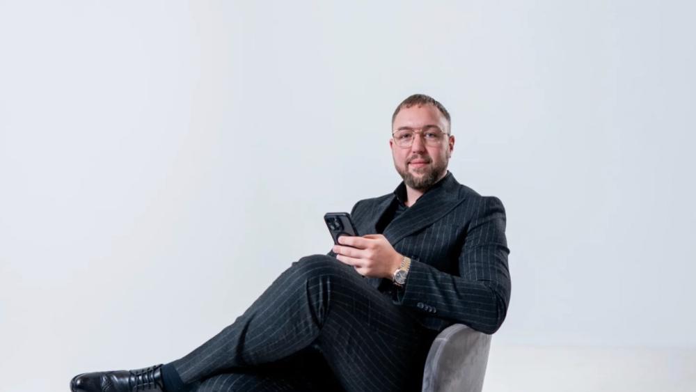 Mann sitzt entspannt mit Smartphone, der über Immobilienkauf nachdenkt.