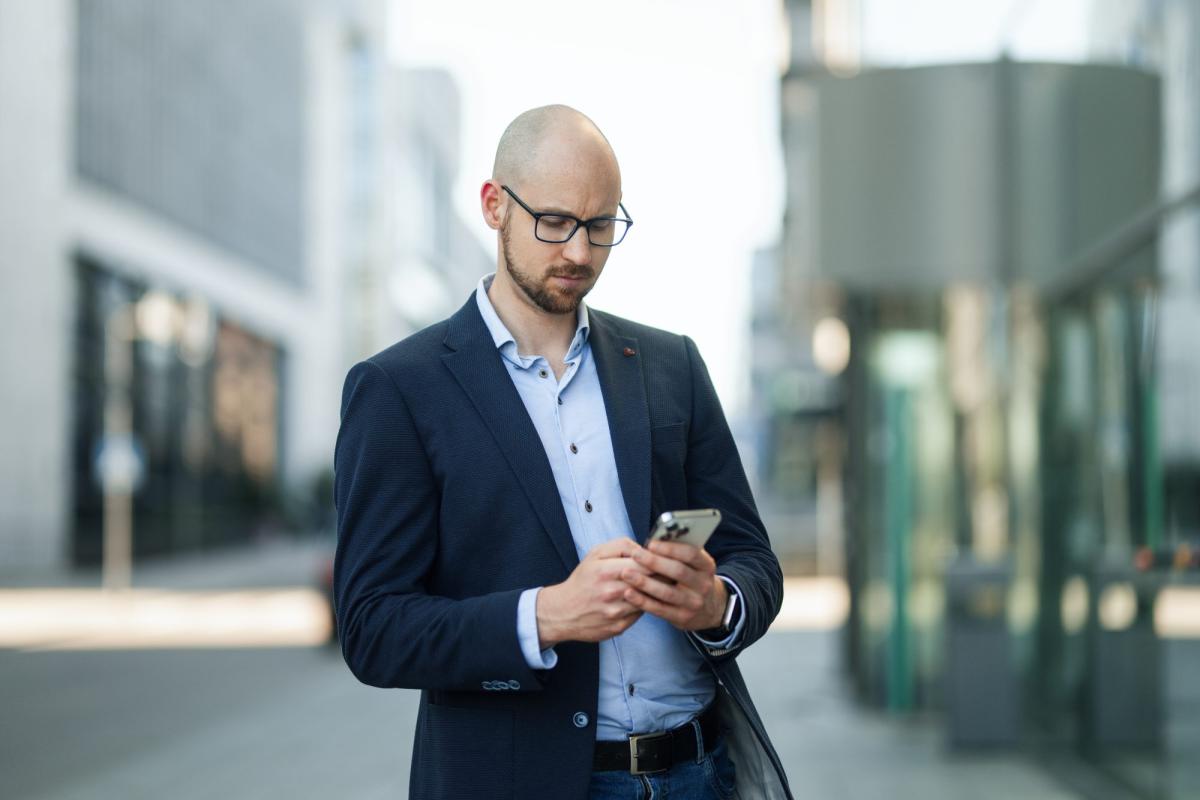 Mann in Anzug prüft sein Handy, während er über die Einstellung eines ersten Mitarbeiters nachdenkt.