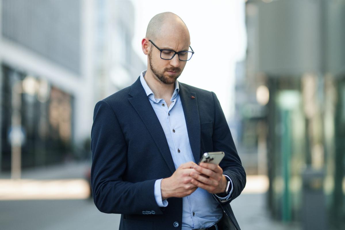 Mann im Anzug mit Smartphone beschäftigt, passend zu Marketing für Sachverständige.