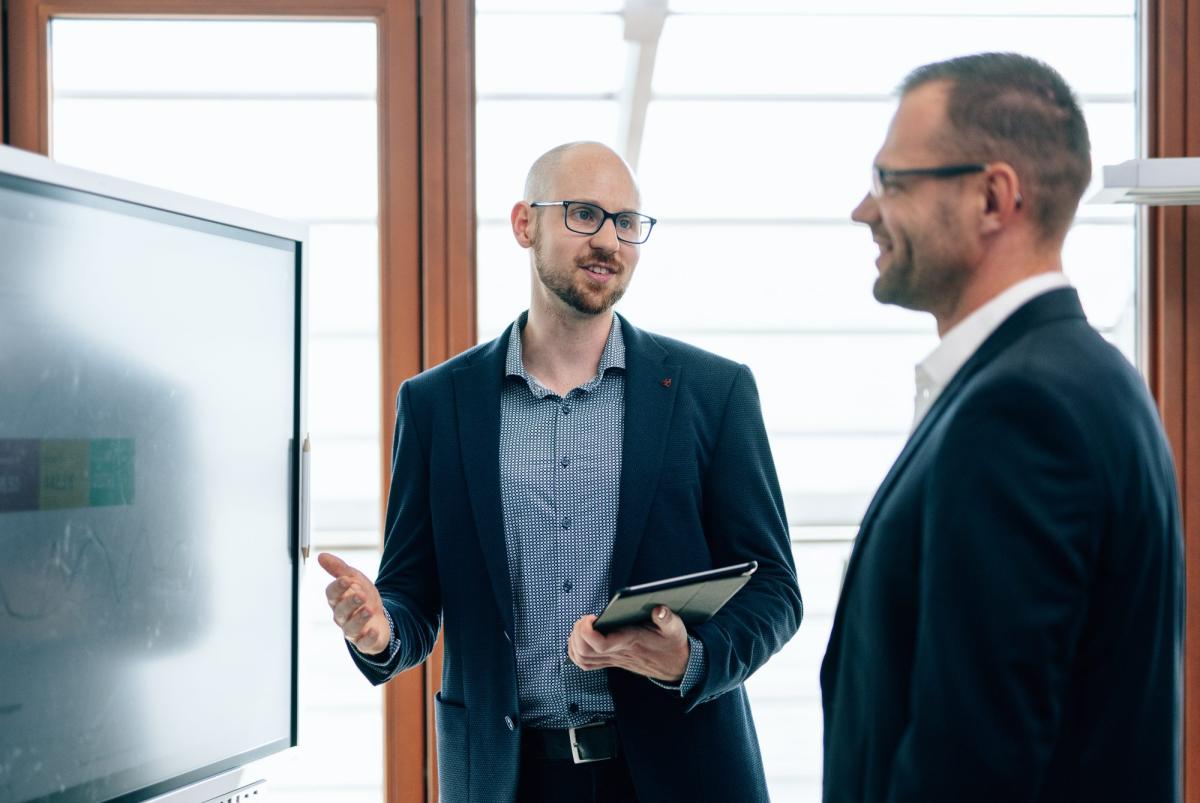 Zwei Männer diskutieren über Branchenbücher als Gutachter in einem modernen Büro.