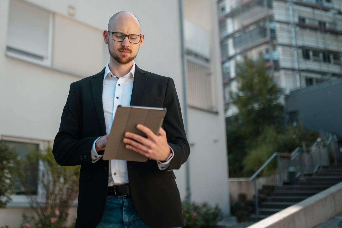 Mann mit Tablet betrachtet Informationen zur DIN ISO 17024 Zertifizierung.
