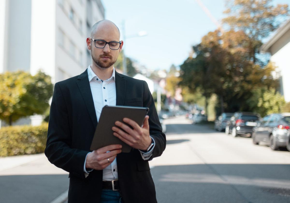 Ein Mann mit Tablet in der Hand, der Sachverständigen-Aufträge planbar macht.