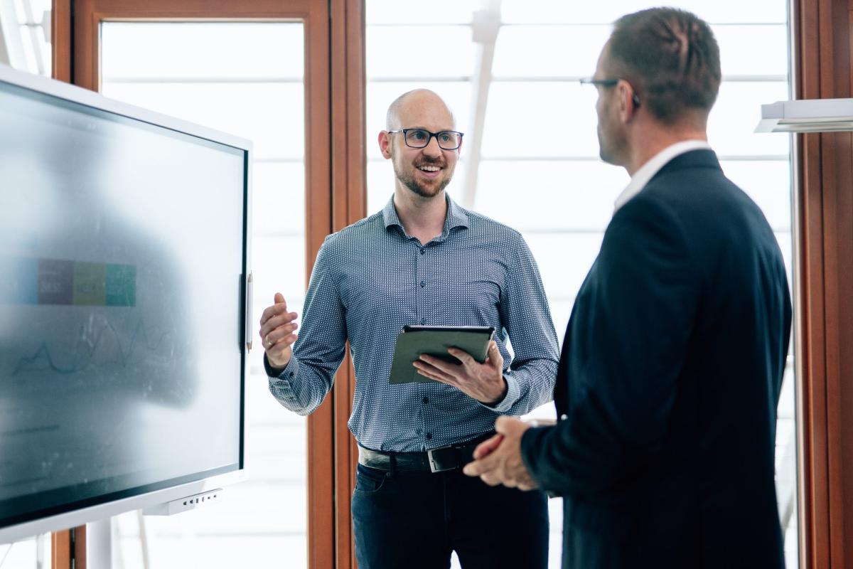 Zwei Männer diskutieren über Online-Marketing für Sachverständige in einem modernen Büro.