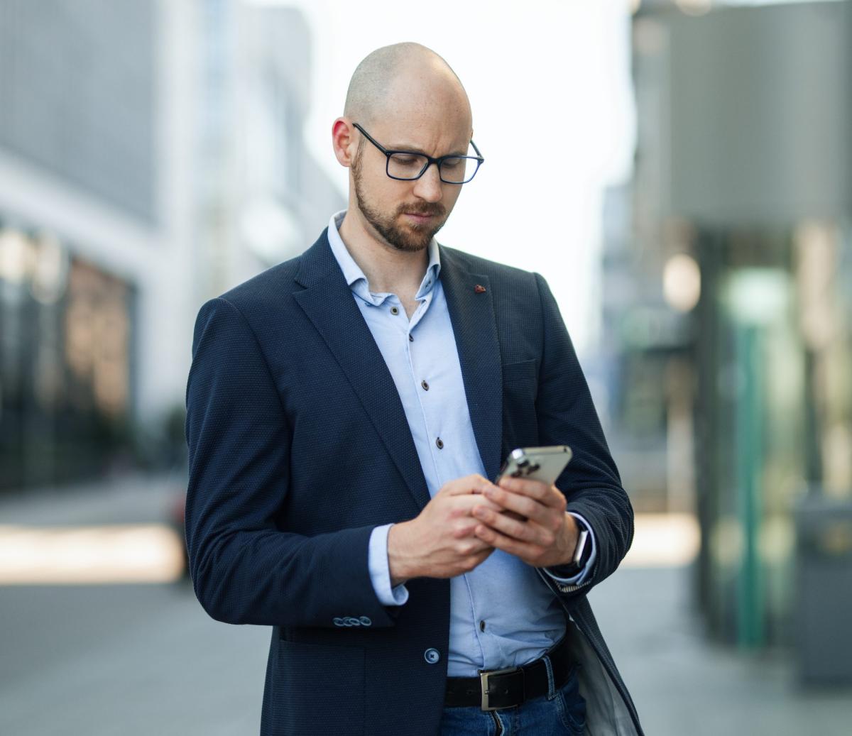Mann im Anzug prüft sein Smartphone auf der Straße, Immobiliengutachter anfragen.