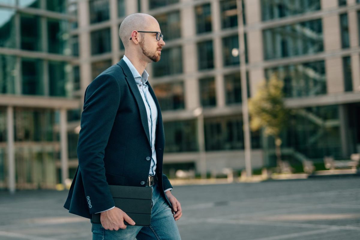 Ein Mann im Anzug geht mit einem Notebook in der Hand, passend zum Thema Gutachterbüro Aufträge Mix.